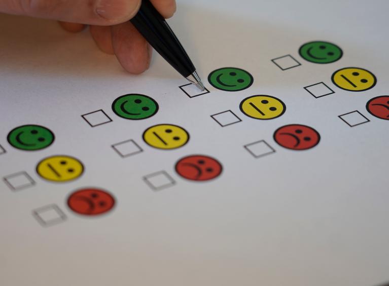 A person completing a feedback survey, about to tick below an image of a green smiling face