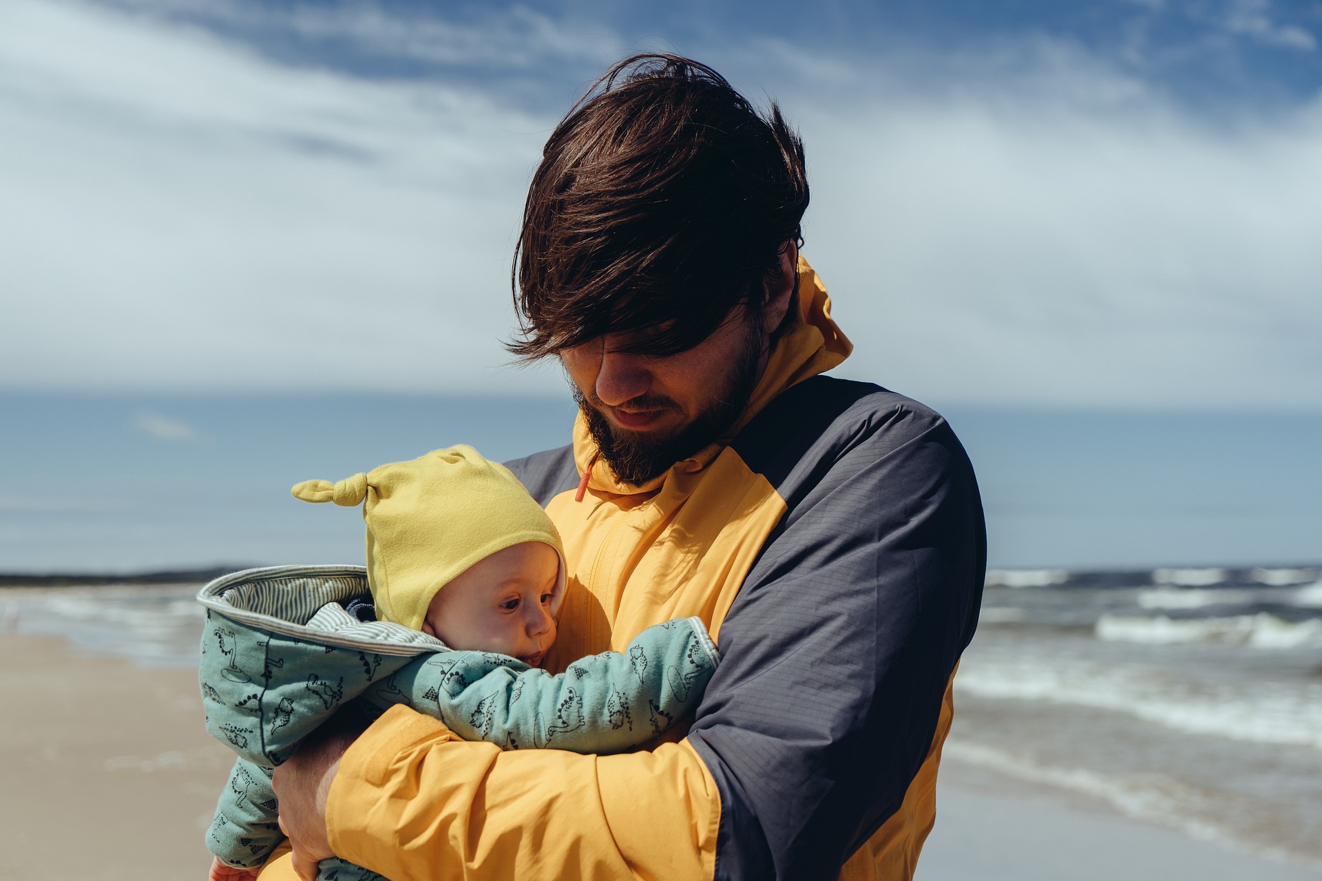 A father holds their baby on a windy beach