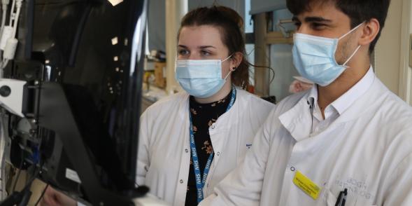 Two pathologists, a woman and a man, look at a display screen 