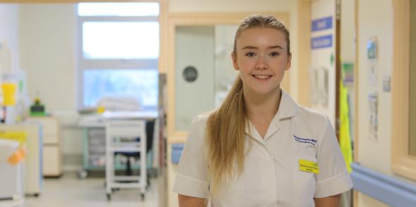 An Intensive Care Unit Dietician smiles whilst standing in a hospital corridor 