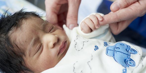 A newborn baby holds onto an adult finger