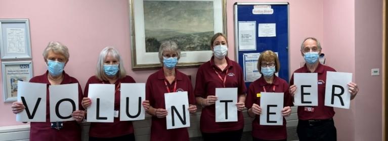 A row of volunteers hold up letters to spell out the word "Volunteer"