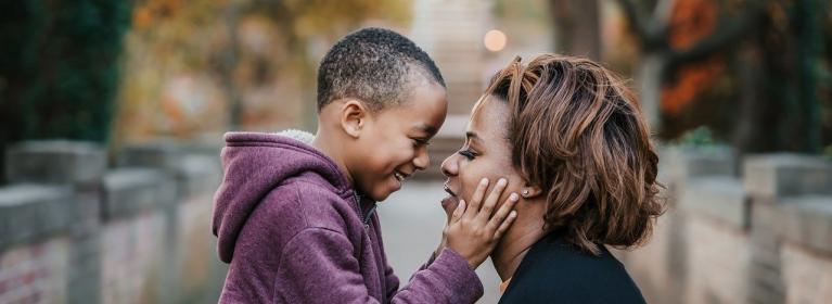 A smiling child holds their mum's face