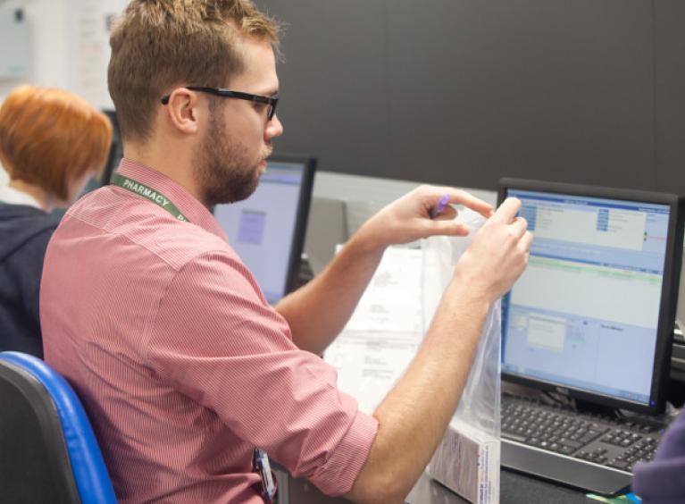 A young man wearing a salmon pink shirt focuses intently as he completes an admin task