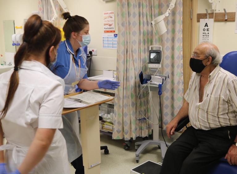 Two members of the nursing team, speak to a patient on a ward