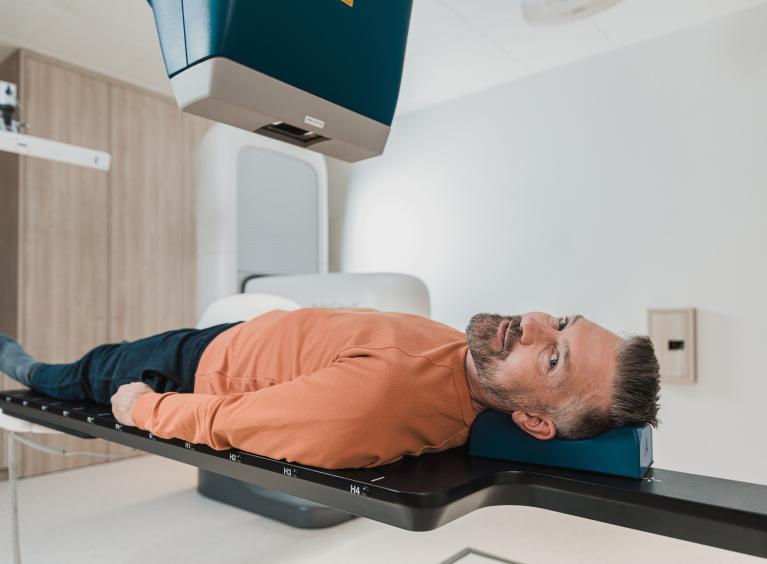 A person looks at the camera whilst they lie on a DXA scanner.