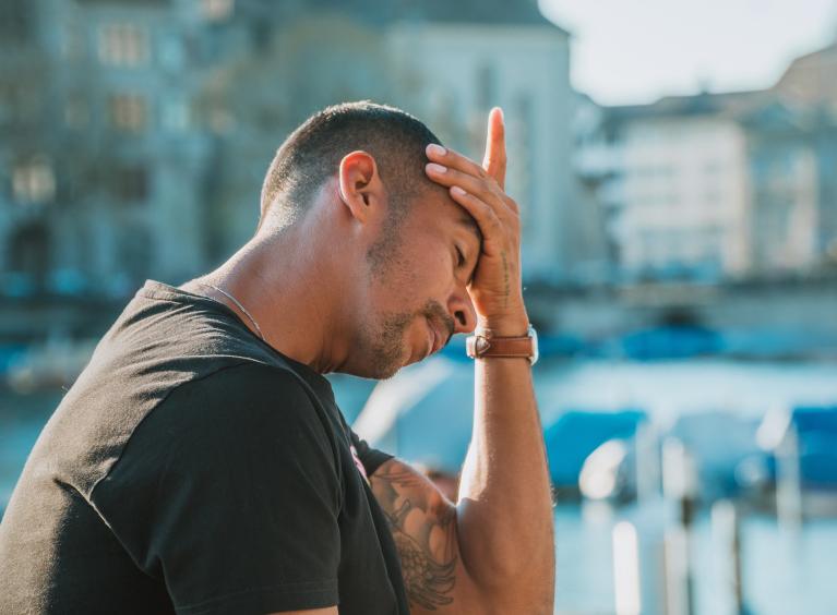 A person rests their head in their hand, as they look downards; they seem stressed and sad.