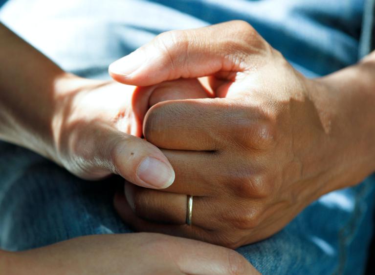 Two people hold hands in a way which suggests worry and stress.
