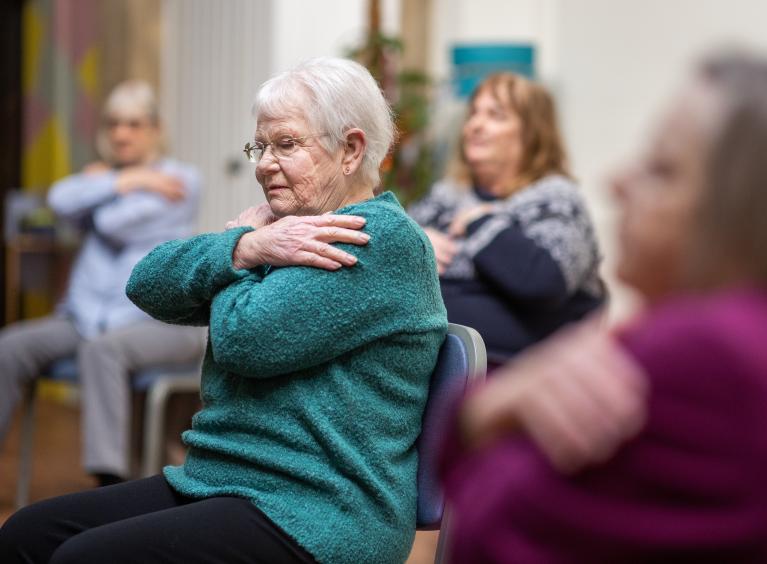 Four older people take part in a group therapy exercise class.