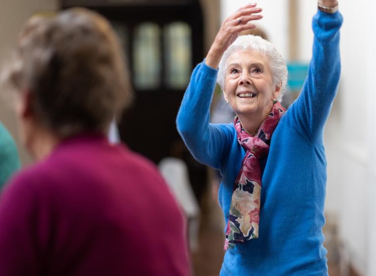 An older woman dances whilst smiling 