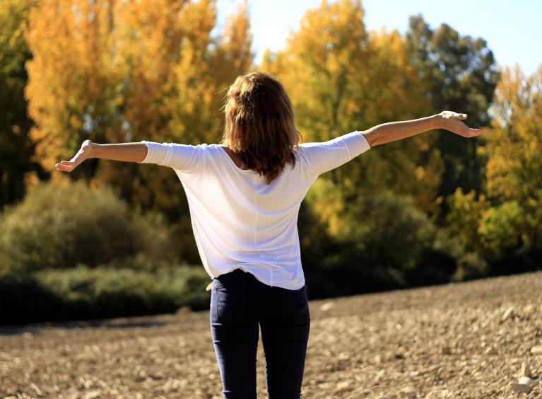 A person stands in a park with their arms outstretched. 