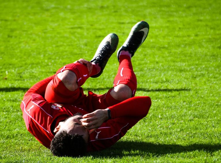 A football player in a red kit, is kneeled over in pain.