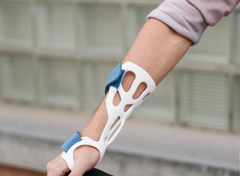 A person rests their hand on the seat of their bike; they are showcasing a splint that they are wearing to support the use of their arm and hand.