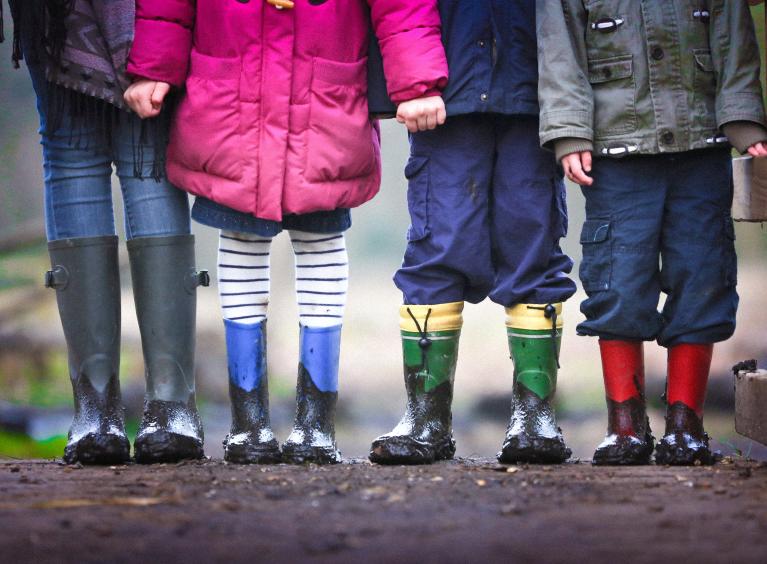 Four children standing together holding hands, wearing wellie boots, outside