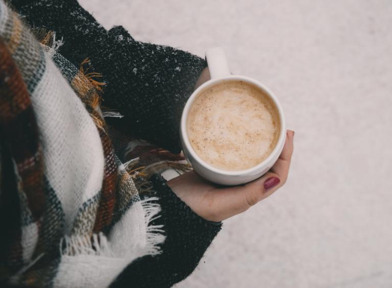 A person holds a hot drink in a cup, whilst standing in snow