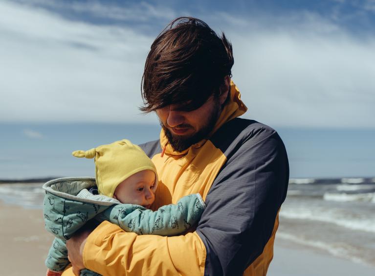 A father holds their baby on a windy beach