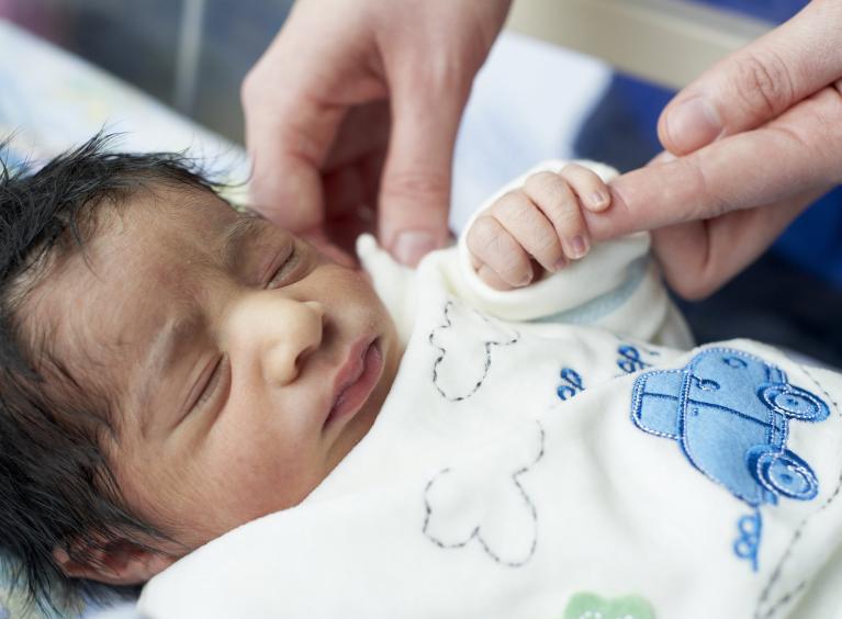 A newborn baby holds onto an adult finger