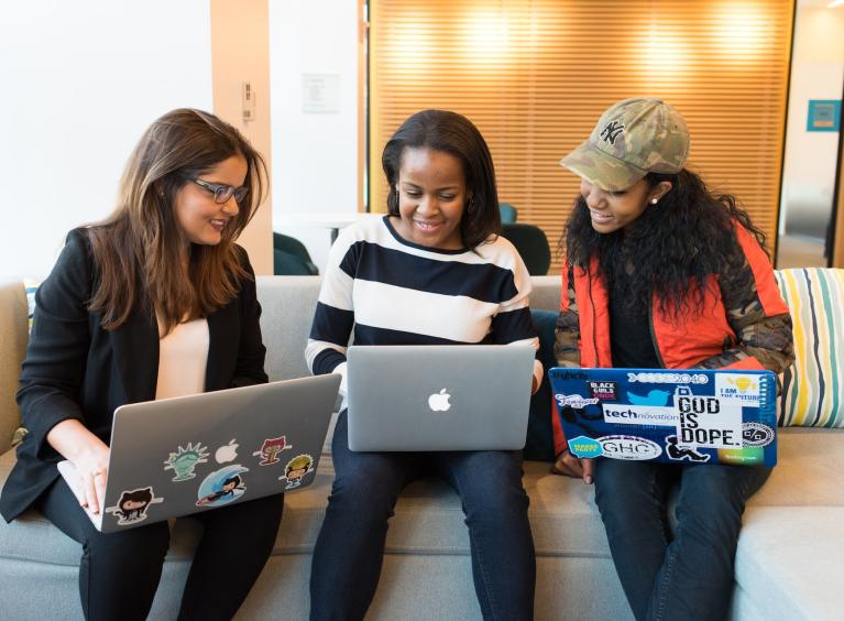 Three women sat together on a sofa looking at their laptops
