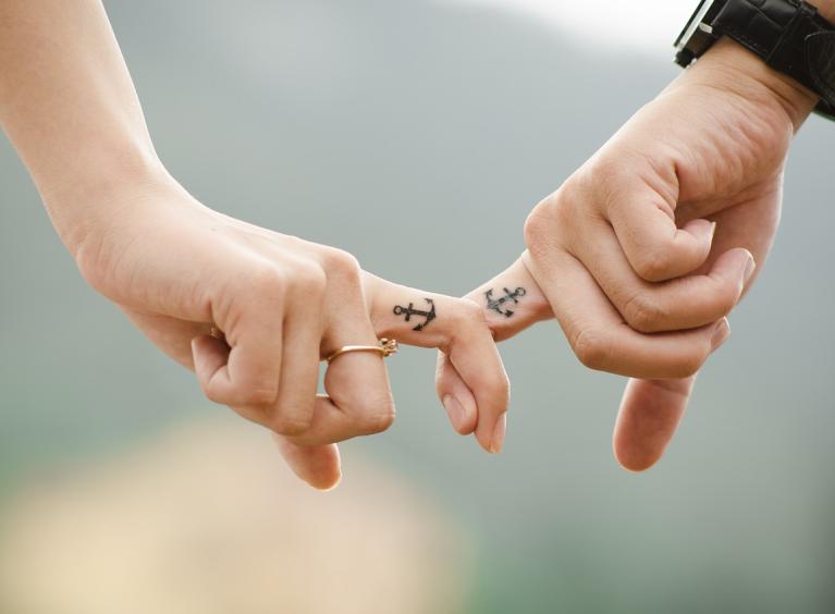 A close up of a couple's fingers linked with matching anchor tattoos on their fingers