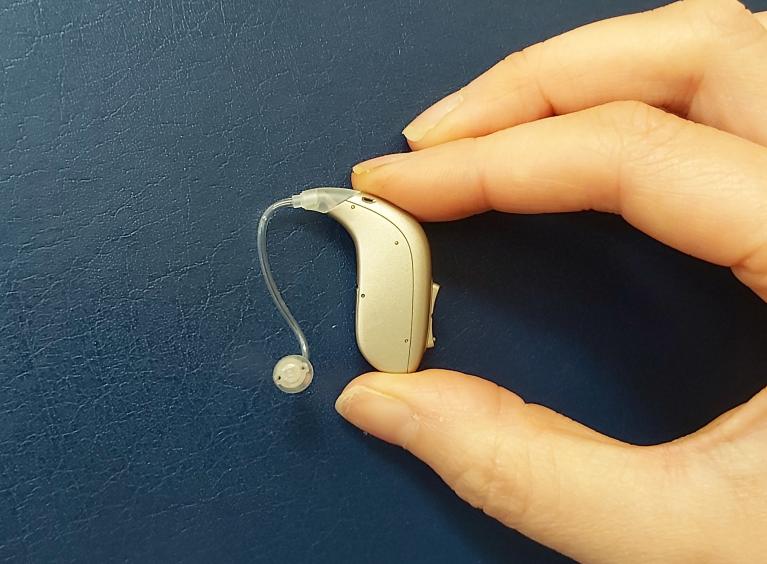 A close up image of a person holding a hearing aid between their thumb and finger