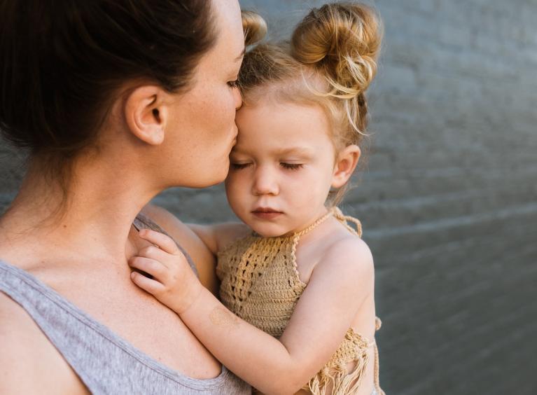 A mother holds her daughter, kissing her on the forehead