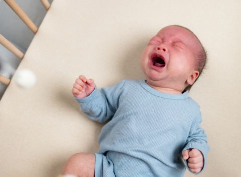 A baby laying on their back in a cot loudly crying