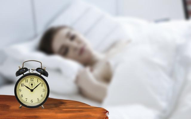 Girl alseep in bed next to an alarm clock